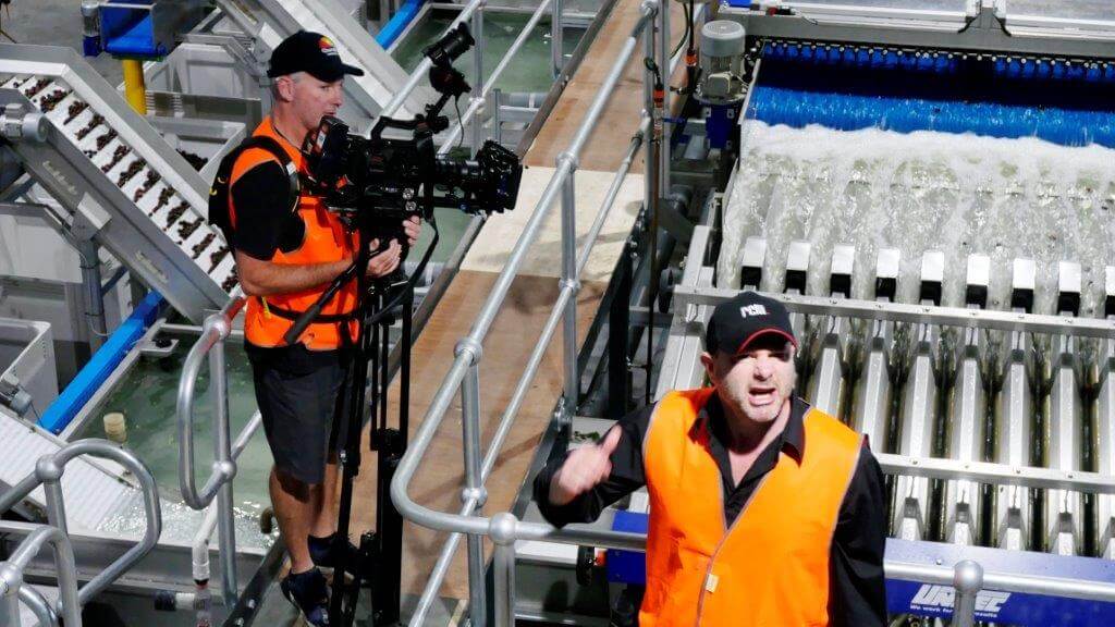 Director yelling directions in a noisy factory with Cameraman in background